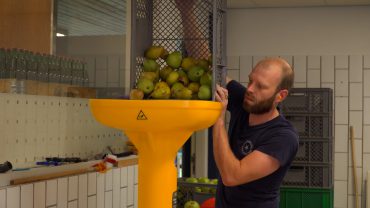 Samen met een collega van De Vergeten Appel is Johan Holleman druk in de weer in zijn productieruimte. Als je binnenstapt in zijn hal in Biezenmortel, is de zoete fruitlucht moeilijk te missen.
